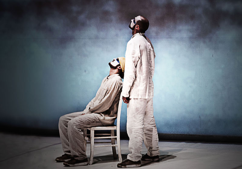 A man sits in a white chair while another hovers over him